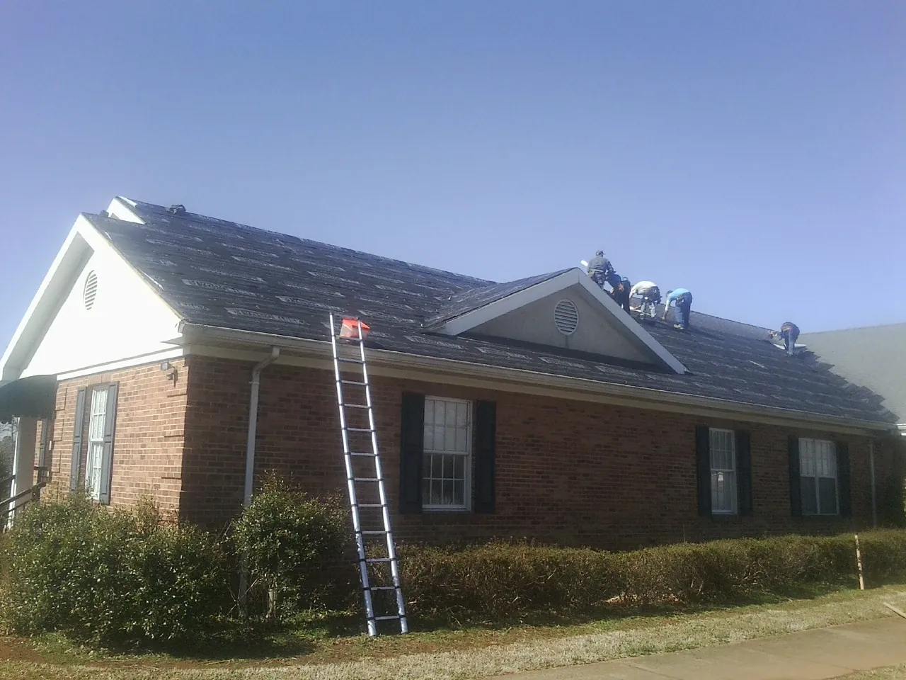 Crew tearing shingles off a brick ranch roof with a ladder set — Metal Roof Repair work by our crew in Glen Lyon