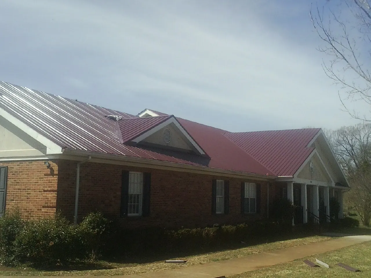 Red metal roof with gabled entries on a long brick building, from a Hail Damage Roof Repair job in Glen Lyon