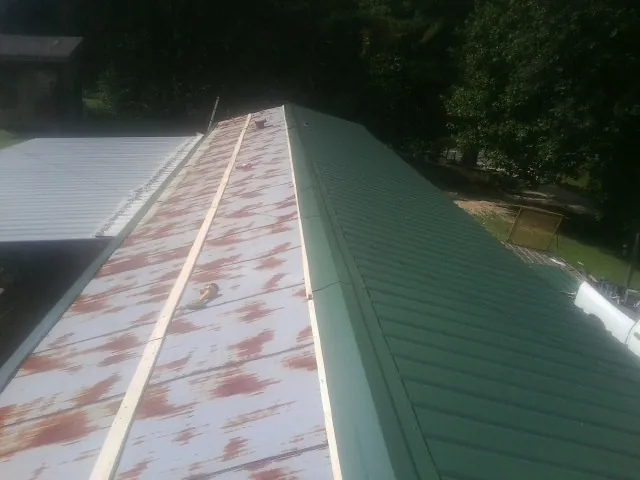 Old rusted panels beside newly installed green metal roofing — Wind Damage Roof Repair by Roofing Brothers in Glen Lyon