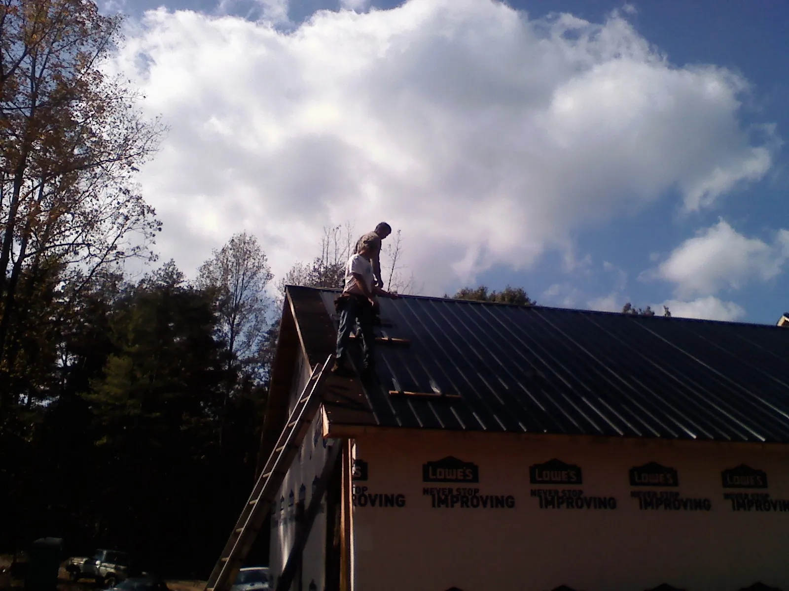 Roofer fastening dark metal panels high against a cloudy sky, from a Roof Inspection job in Glen Lyon