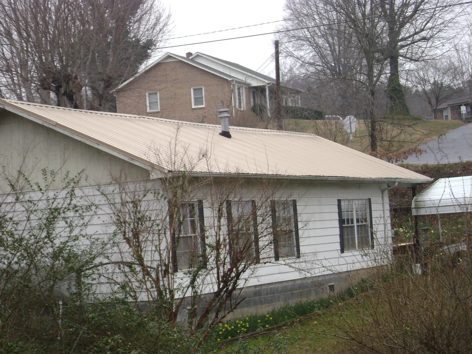 Tan metal roof on a white sided house set into a hillside — Commercial Roofing by Roofing Brothers in Glen Lyon